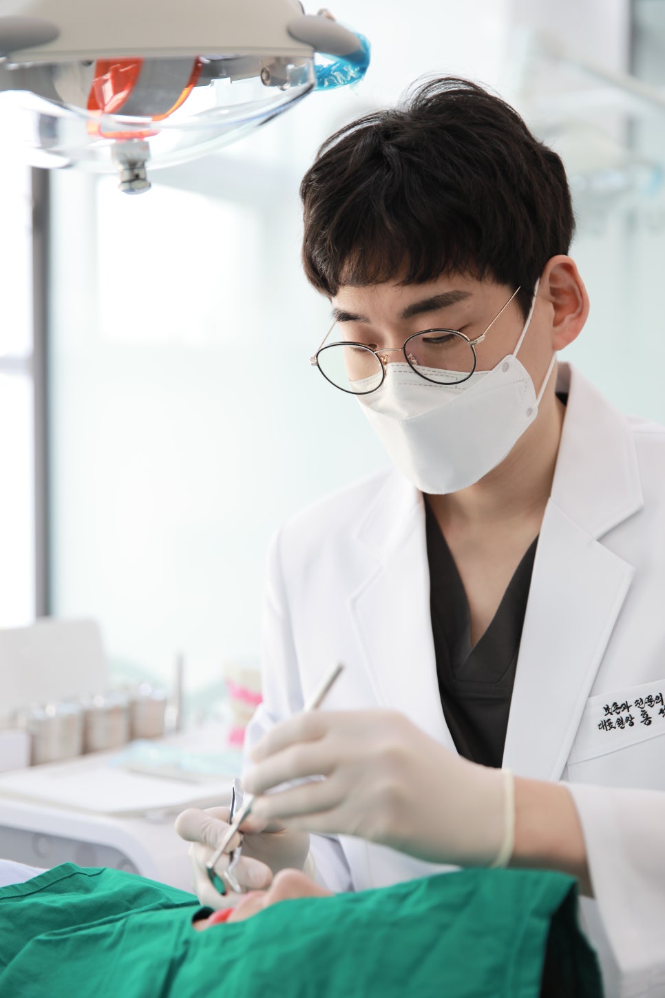 마스크를 착용한 치과의사가 환자의 구강을 진료하는 모습. 치과용 기구를 사용하고 있다.