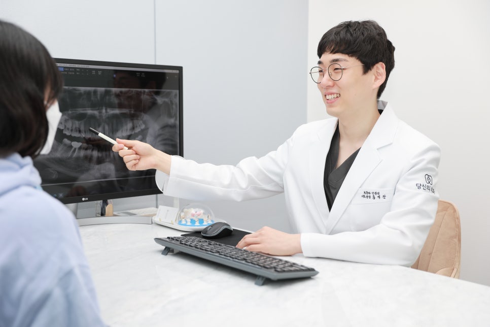 치과의사가 환자에게 모니터에 보이는 엑스레이 사진을 가리키며 설명하는 모습