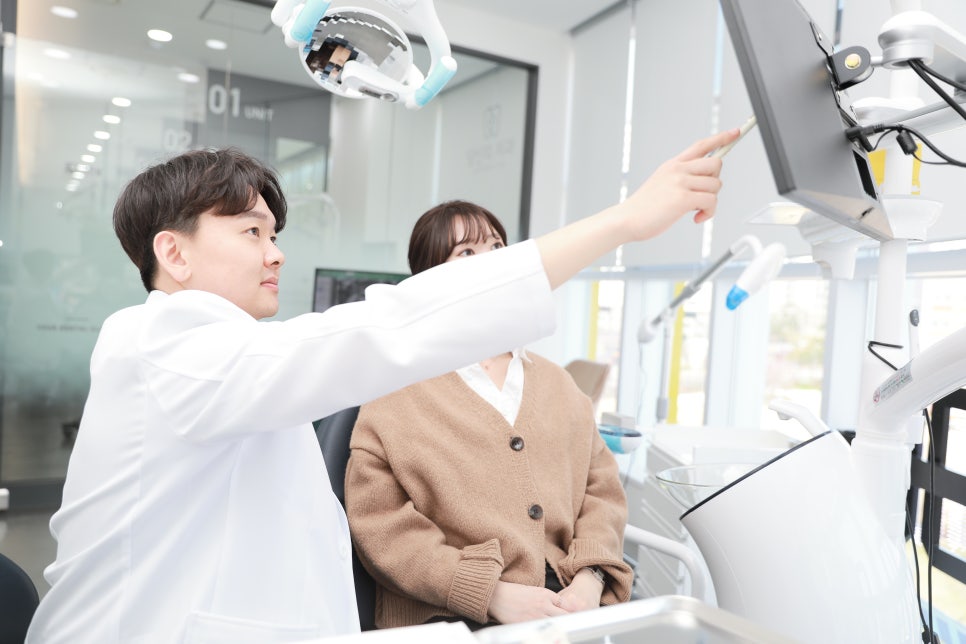 치과 진료실에서 의사가 환자와 함께 모니터를 보며 설명하는 모습