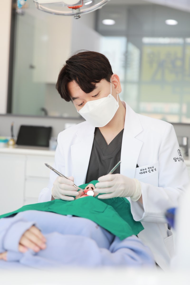 마스크를 쓴 치과의사가 환자의 구강을 진료하는 모습
