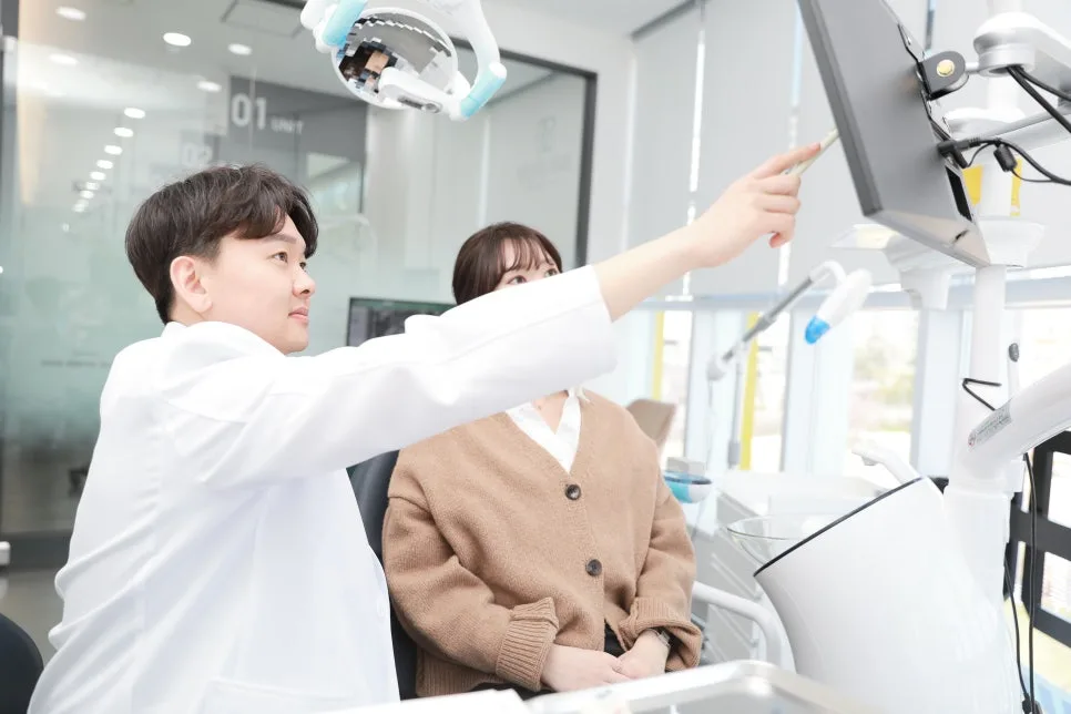 치과 의사가 환자와 함께 모니터를 보며 손가락으로 가리키며 설명하는 모습