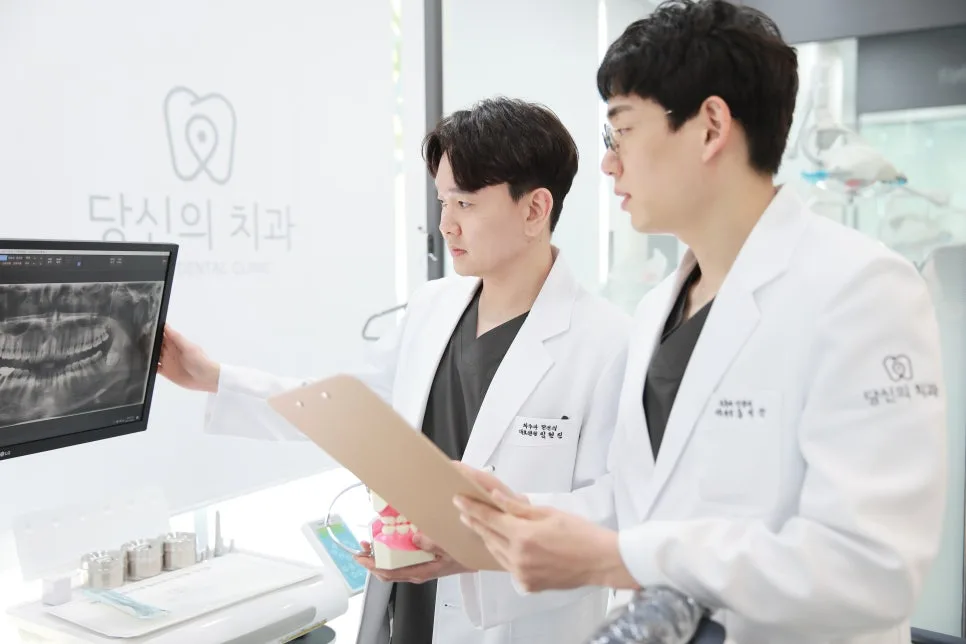 두 명의 치과 의사가 모니터의 파노라마 방사선 사진을 보며 진료 계획을 논의하는 모습