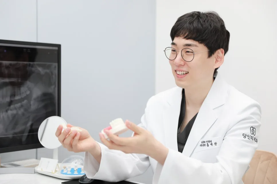 치과 의사가 치아 모형을 들고 환하게 웃으며 설명하는 모습